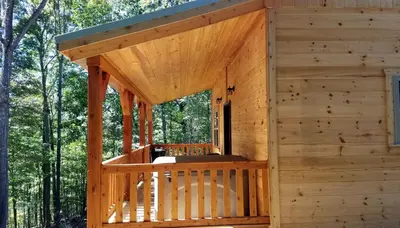 a wooden cabin with a porch in the woods at Cozy Family-Friendly Cabin with Private Outdoor Jacuzzi near Huntington, West Virginia in Genoa