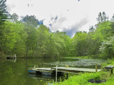 a dock on a lake with trees and clouds in the sky at Magnificent A-Frame Cabin Rental in the Trees close to Hocking Hills State Park, Ohio in Laurelville