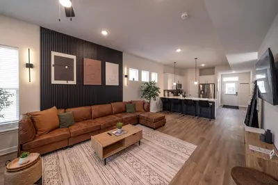 a living room with a brown couch and a kitchen at Arcade Game Room! Luxury New 3BR CLE Clinic UnivCircle Little Italy in Cleveland