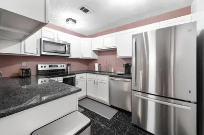 a kitchen with white cabinets and a stainless steel refrigerator at Cozy Condo On Collins- Walk to High St /Dtown /OSU in Columbus