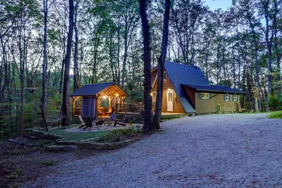 a wooden cabin in the woods with a tent at Hocking Hills Social Distance Cabin with Hot Tub in Laurelville