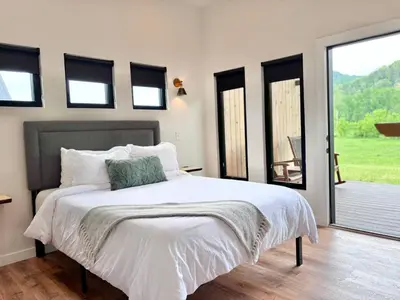 a bedroom with a bed with white sheets and windows at Three Suns Full Rental | 8 Cabins | Views | River in Stanton