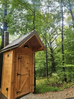 a wooden outhouse with a door in the woods at Lovely Rural Cabin Nestled Among Nature by Tappan Lake in Ohio in Deersville
