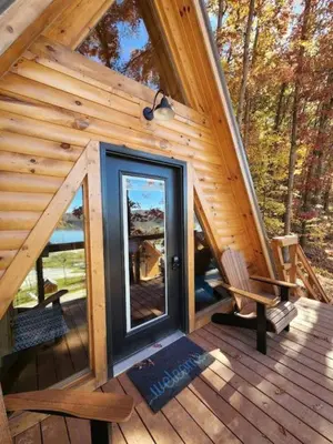 a cabin with a glass door on a deck at Rustic Tree A-Frame with Original Design by Tappan Lake in Ohio in Deersville