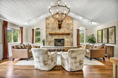 a living room with a stone fireplace and a chandelier at Cozy Secluded Cabin with Games and Hot-tub in Sarahsville, Ohio