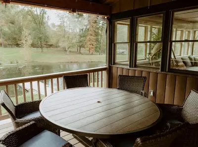 a wooden table and chairs on a screened in porch at 16 Guests | Ponds | Hot Tub | Game Room | Trails in Sarahsville