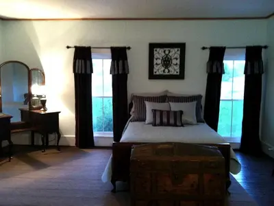 a bedroom with a bed and a table and windows at 1800s Farmhouse Cottage Rental on a 230 Acre Farm in Muskingum County, Ohio in Frazeysburg