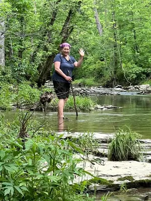 a woman standing in a river with a stick at Magical Family Tree House in Secluded Woodland near Germantown, Kentucky in Germantown