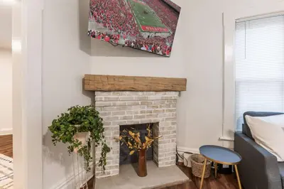 a living room with a brick fireplace with a picture of a baseball game at Steps 2 High ST - BIG Patio - Private parking- OSU in Columbus
