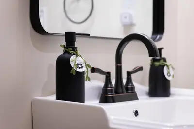 a bathroom sink with a black bottle with a flower on it at ADA Suite - Room 6 in Versailles