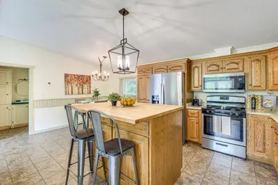 a kitchen with wooden cabinets and a island with bar stools at Walk to River Loudonville Retreat with Hot Tub! in Loudonville