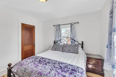 a bedroom with a bed with a purple comforter and a window at Cozy Getaway with Hot Tub, Patio & Fenced Yard home in Garfield Heights