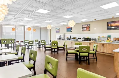 a dining room with tables and green chairs at Suburban Studios Charleston - Civic Center in Charleston