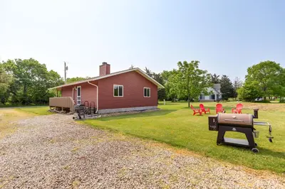 a red house with chairs and a grill in the yard at Walk to Lake Kelleys Island Gem with Deck! in Kelleys Island