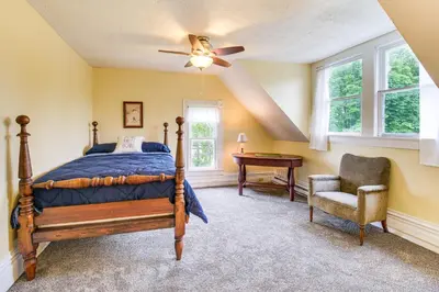 a bedroom with a bed and a chair and a ceiling fan at 2 Mi to Chardon Square Spacious Farmhouse in Concord
