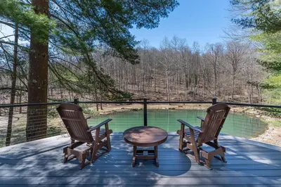 two chairs and a table on a deck with a pond at Spring Mountain Cove in Warsaw