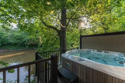 a hot tub on a deck next to a river at White Oak Cottage in Mount Orab