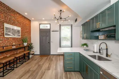 a kitchen with green cabinets and a brick wall at Mansfield Retreat - A Chic Downtown Experience in Cincinnati