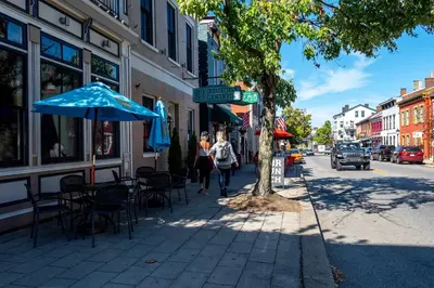 a woman walking down a sidewalk with an umbrella and tables and chairs at Heart of Mainstrasse 1 in Covington