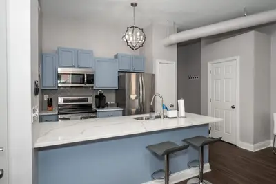 a kitchen with blue cabinets and a sink and two bar stools at Heart of Mainstrasse Suites in Covington