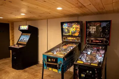 three video game machines are lined up in a room at Pet-Friendly Tree Cabin by Tappan Lake with Lofted Space in Ohio in Deersville