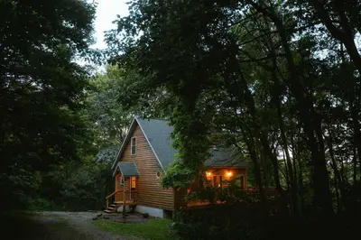 a cabin in the woods with the lights on at Cheerful Two Bdrm Cabin with Hot Tub & Pet Friendly in Rockbridge
