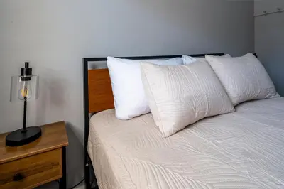 a bed with white pillows and a table with a lamp at Cozy 2BR Retreat with Workspace - Washer and Dryer in Kettering