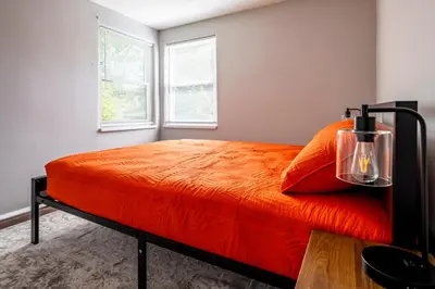 a bedroom with a bed with an orange blanket and two windows at Relaxed 2BR Apt in Moraine with Office Space and Washer & Dryer in Moraine