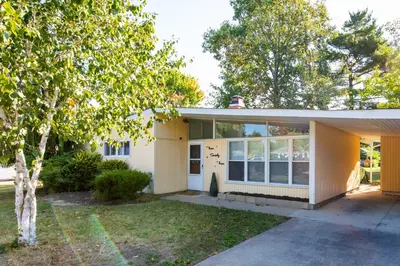 a yellow house with a tree in front of it at Mid-Century Modern Themed Home with Outdoor Hot Tub in Vermilion