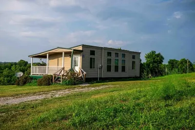 a mobile home on a grassy field next to a house at Rustic Mt Sterling Cabin1 Near Downtown Pets OK in Mount Sterling