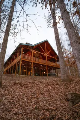 a large wooden building in the middle of trees at Sleeps 16! Luxury Cabin with Game Room & Hot Tub in Nelsonville