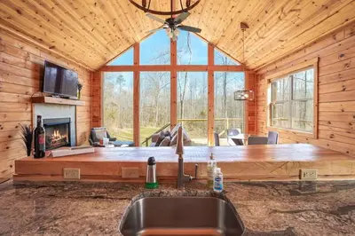 a kitchen with a sink and a fireplace in a log cabin at Fern Haven A modern take on Hocking Hills cabins in McArthur