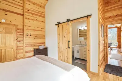 a bedroom with a white bed and wooden walls at Fern Haven A modern take on Hocking Hills cabins in McArthur