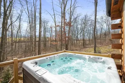 a hot tub on a deck with a view of the woods at Fern Haven A modern take on Hocking Hills cabins in McArthur