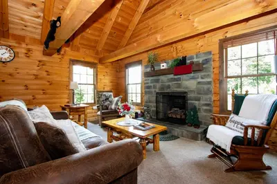 a living room with a stone fireplace in a log cabin at Honey Bear Cabin in Millersburg