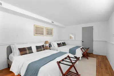 two beds in a bedroom with white walls and wood floors at Spacious 5BR Firepit with Deck Near OSU and More in Columbus