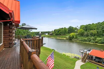 a wooden deck with an american flag and a river at Lakeside Log Home, Private Dock, Near Ark! in Dry Ridge