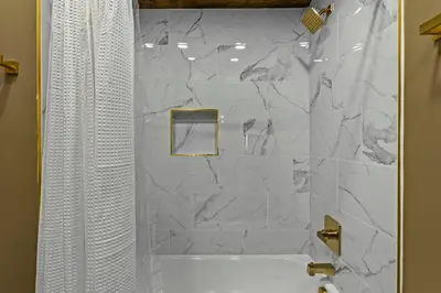 a bathroom with a shower with a white marble wall at New Barn/ Sleeps 12/ 2 Hot Tubs/ EV Charger in Stanton