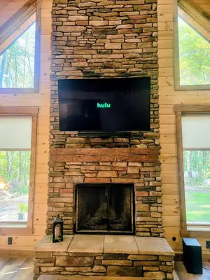 a living room with a stone fireplace with a flat screen tv at WildWood Cabin in Gambier
