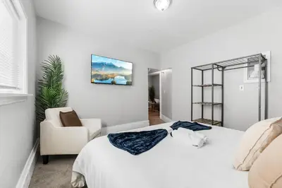 a white bedroom with a bed and a chair at Little Italy Family Suite 4 TVs Bunk Beds in Cleveland