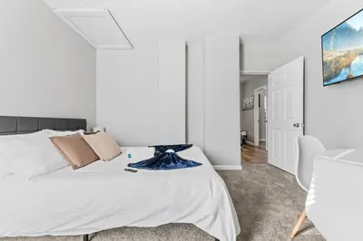 a white bedroom with a large bed and a chair at Little Italy Family Suite 4 TVs Bunk Beds in Cleveland