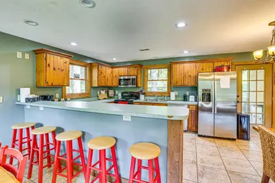 a kitchen with wooden cabinets and a counter with red stools at 23 Mi to Mohican SP Group-Ready Lodge with Hot Tub in Brinkhaven