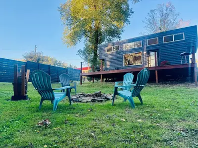 a group of three chairs sitting in the grass in front of a house at Creekside Haven Tiny Home