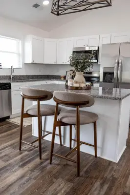 a kitchen with white cabinets and a counter with stools at Creek View Cottage