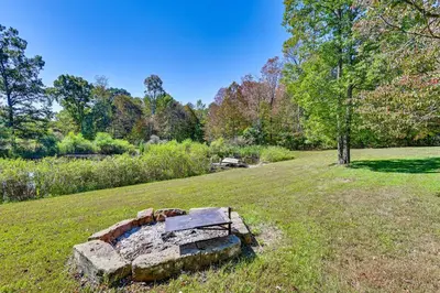 a stone bench in a field with trees in the background at Ohio Hunters Cabin with Pond Access Pets Welcome!