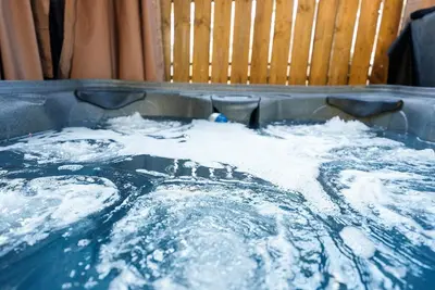 a hot tub filled with water next to a wooden chair at Cozy escape with Hot Tub, ideal for family & friends in Columbus