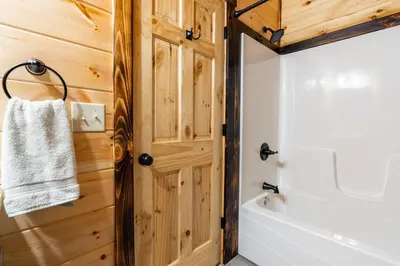 a bathroom with a white tub and a wooden wall at Cheerful Cabin Nestled in Serene Wooded Ravine in Logan