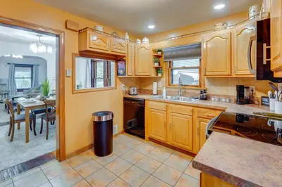 a kitchen with wooden cabinets and a dining room at 1 Mi to Akron Zoo Ranch-Style Home with Yard! in Akron
