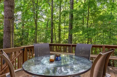 a table and chairs on a deck with trees at Sugar Shack - Cave Run Lake OR Red River Gorge KY in Bangor