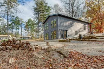 a gray house with a pile of logs at Chène Cottage Near Burr Oak Lake and Trailheads! in Glouster